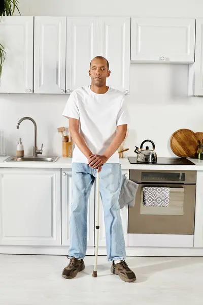 Ein afroamerikanischer Mann mit Stock steht selbstbewusst in einer Küche und demonstriert Stärke und Widerstandskraft. — Stockfoto