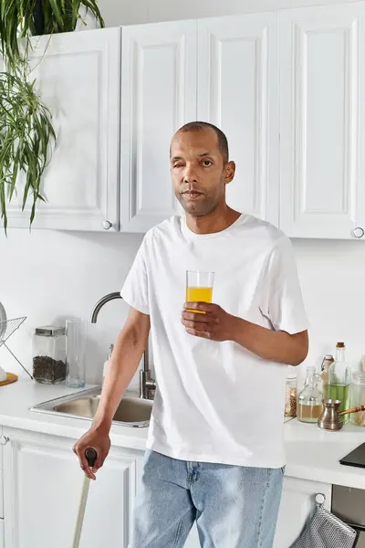 Ein afroamerikanischer Mann mit Myasthenia-Gravis-Syndrom steht in einer Küche und hält ein Glas Orangensaft in der Hand. — Stockfoto