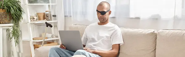An African American man with Myasthenia Gravis syndrome is sitting on a couch, using a laptop, with his Labrador dog nearby. — Stock Photo