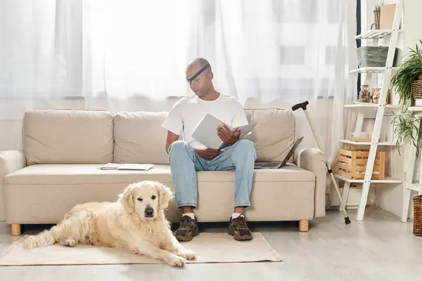 Um homem afro-americano deficiente com síndrome da miastenia gravis relaxa em um sofá ao lado de seu cão Labrador leal. — Fotografia de Stock
