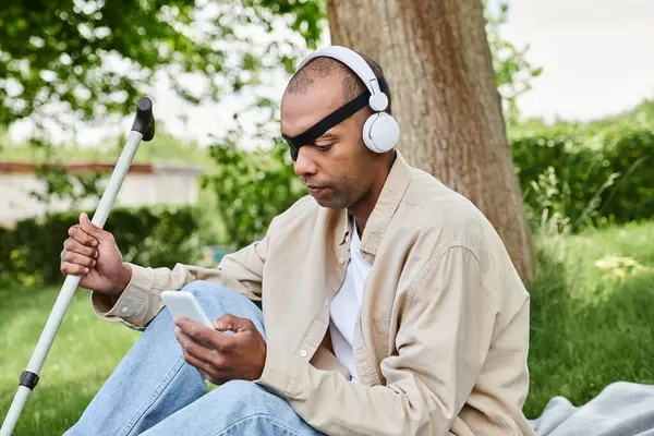 Афроамериканец с синдромом миастении грависа расслабляется на траве в наушниках, обнимая музыку. — стоковое фото