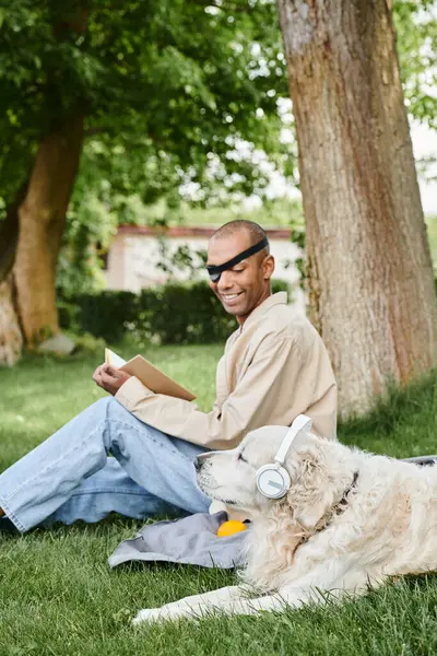 A man with myasthenia gravis syndrome sits with his Labrador dog in the grass, both wearing headphones. — Stock Photo