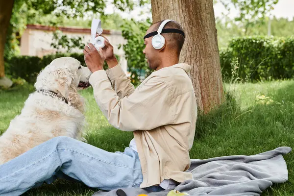 Инвалид афроамериканец с синдромом миастении и грависа сидит на траве рядом с лояльной собакой-лабрадором.. — стоковое фото