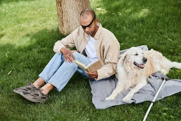 Um homem afro-americano com síndrome de Myastenia Gravis lendo um livro sobre um cobertor com seu cão Labrador. — Fotografia de Stock