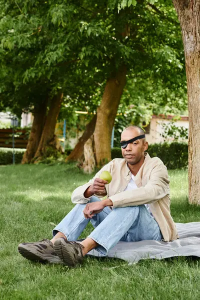 Un hombre con síndrome de miastenia grave se sienta en una manta en la hierba, disfrutando del aire libre. - foto de stock