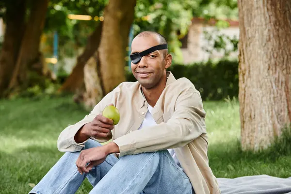 Un afroamericano discapacitado se sienta pacíficamente sobre una manta, acunando una manzana en sus manos - foto de stock