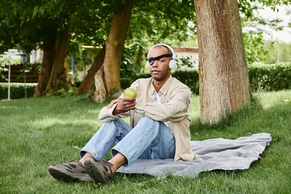 Ein afroamerikanischer Mann mit Myasthenia-Gravis-Syndrom sitzt auf einer Decke in einem ruhigen Grasfeld. — Stockfoto