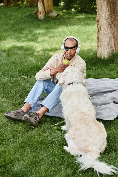 Un hombre sentado en la hierba junto a un perro labrador, que encarna la diversidad y la inclusión. - foto de stock
