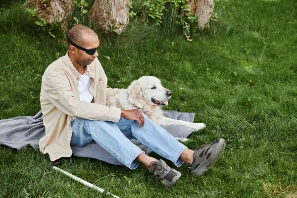 Um homem afro-americano deficiente com síndrome da miastenia gravis senta-se na grama com seu cão Labrador leal. — Fotografia de Stock
