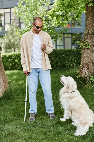 Un uomo afroamericano con miastenia gravis si trova accanto a un labrador bianco leale su un prato verde vibrante. — Foto stock