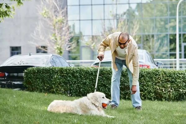 Un afroamericano discapacitado con miastenia gravis juega felizmente con su perro labrador en la exuberante hierba verde. - foto de stock