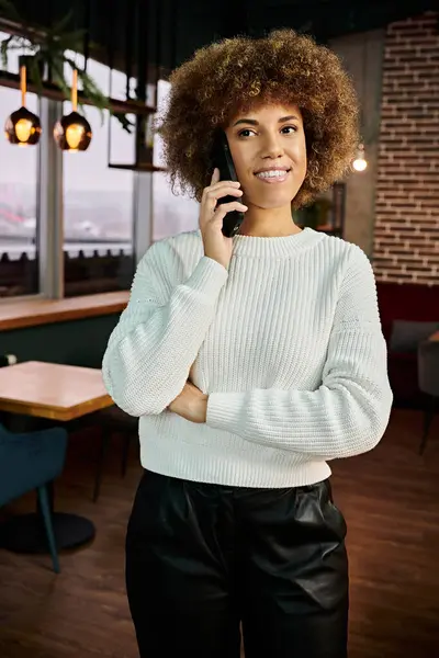 An African American woman standing in a modern restaurant, engaged in conversation on a cell phone. — Stock Photo