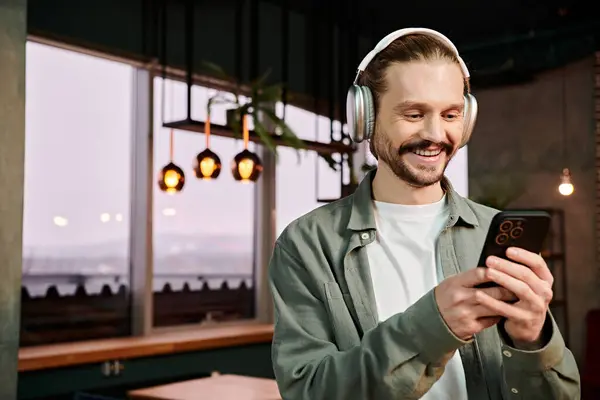 A man, wearing headphones, gazes at his phone in a modern cafe while connected to music. — Stock Photo