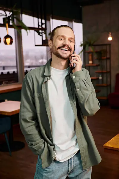 Un homme, dans un restaurant moderne, parle animément sur son téléphone portable tout en se tenant au milieu de l'atmosphère animée. — Photo de stock