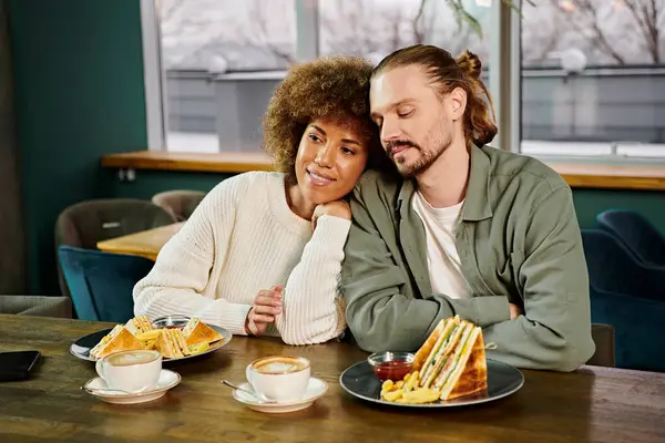 An African American woman and a man are seated at a table, sharing a meal in a modern cafe setting. — Stock Photo