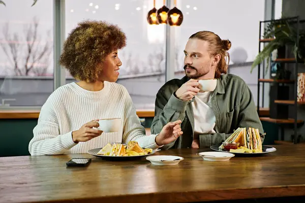 Una donna afroamericana e un uomo gustare un pasto insieme a un tavolo in un caffè moderno. — Foto stock