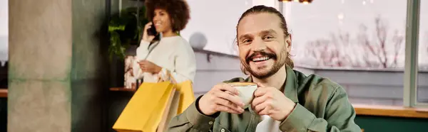 Um homem sentado em uma mesa, desfrutando de uma xícara de café em um café moderno. — Fotografia de Stock