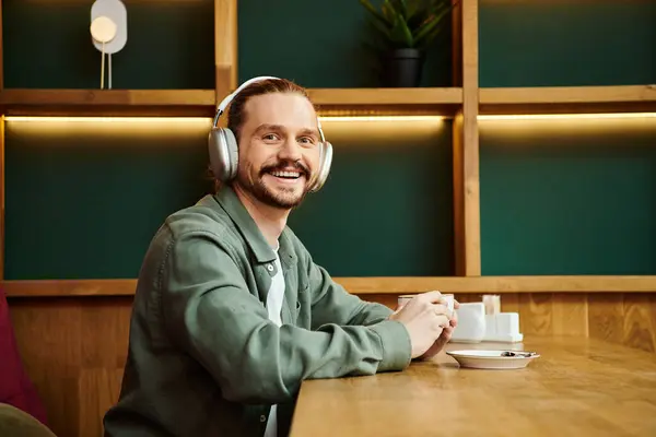 Man sitting at a table, engrossed in music with headphones on in a modern cafe setting. — Stock Photo