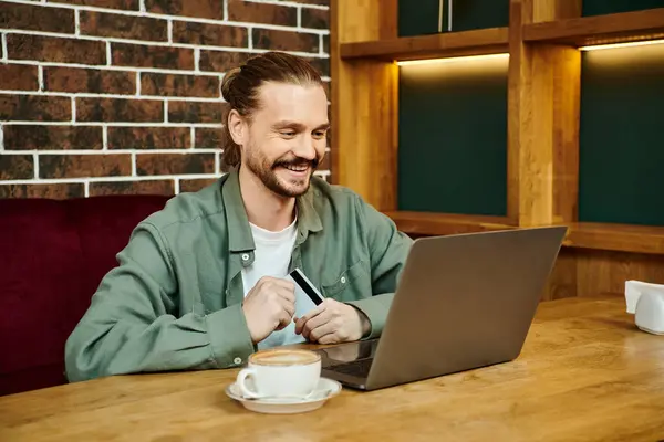 Un hombre se sienta en un café moderno, centrado en la pantalla de su computadora portátil, dedicado a actividades de trabajo o de ocio. - foto de stock