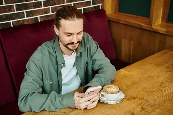 A man sits at a table, savoring a cup of coffee in a modern cafe and using smartphone — Stock Photo