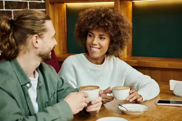 Eine afroamerikanische Frau und ein Mann sitzen an einem Tisch und genießen Tassen Kaffee in einem modernen Café-Ambiente. — Stockfoto