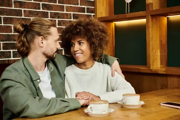 An African American woman and man sit at a table, enjoying cups of coffee in a modern cafe setting. — Stock Photo