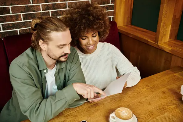 Uma mulher e um homem afro-americanos sentam-se à mesa, escolhendo a refeição no menu de um café moderno. — Fotografia de Stock