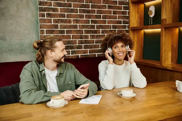 Una mujer afroamericana y un hombre absortos en conversaciones de teléfono celular mientras están sentados en una mesa de café. - foto de stock