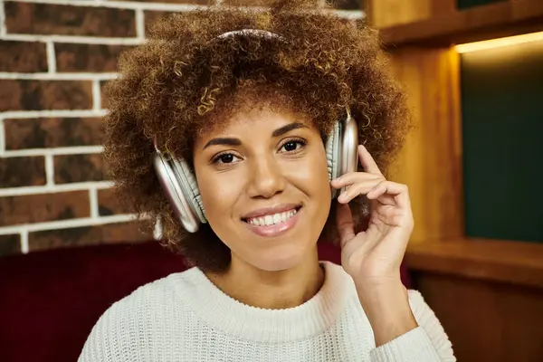 An African American woman wearing headphones in a modern cafe, immersed in music. — Stock Photo