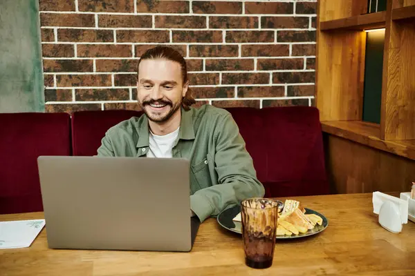 Мужчина сидит за столом, сосредоточенный на ноутбуке, в современном кафе. — стоковое фото