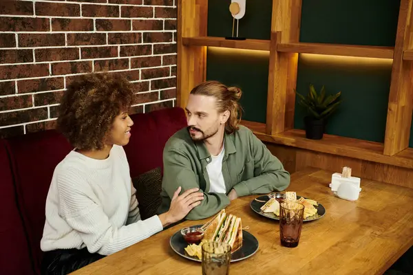 Афроамериканка и мужчина сидят вместе за столом, наслаждаясь едой в современном кафе. — стоковое фото