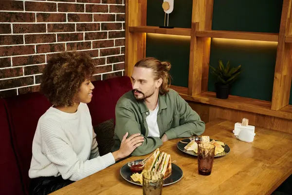 Uma mulher afro-americana e um homem sentam-se juntos em uma mesa, desfrutando de uma refeição em um café moderno. — Fotografia de Stock