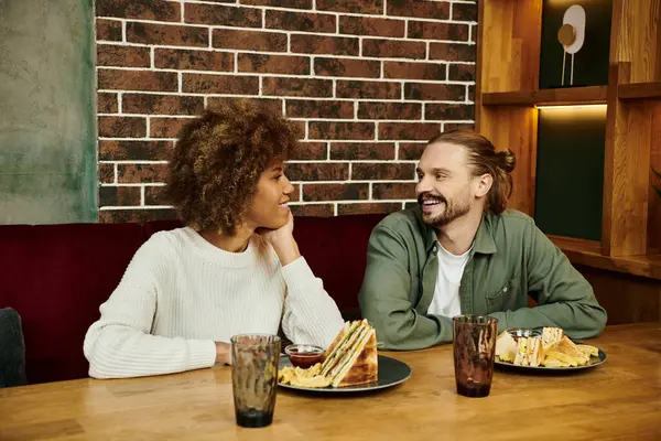 Une femme afro-américaine et un homme dégustent un repas ensemble à une table dans un café moderne. — Photo de stock