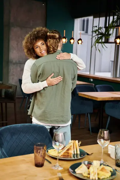 African American woman and man hug tightly in trendy cafe, sharing a moment of warmth and affection amidst bustling ambiance. — Stock Photo