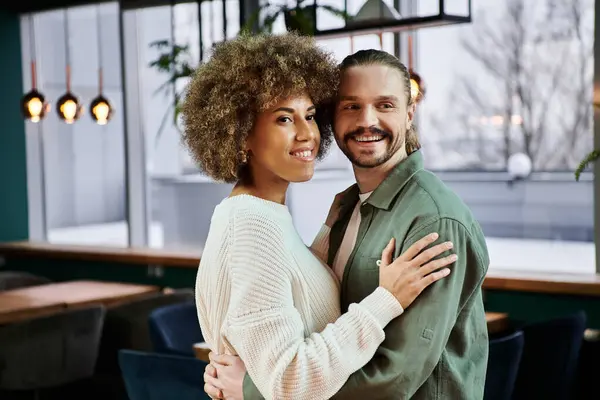 An African American woman and a man share a heartfelt embrace in a modern restaurant setting. — Stock Photo