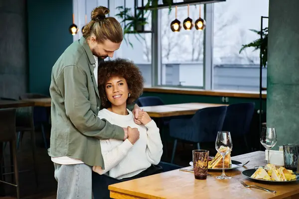 A woman with curly hair and a man sit together in a modern cafe, engaged in conversation and hug — Stock Photo