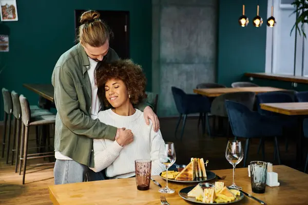 Una mujer afroamericana abraza a un hombre en un acogedor restaurante lleno de decoración moderna. - foto de stock