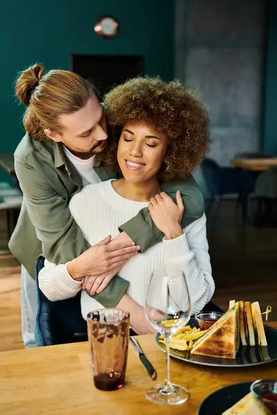 Африканська американка і чоловік поділяють сердечні обійми за столом в сучасному кафе, висловлюючи любов і зв'язок. — стокове фото