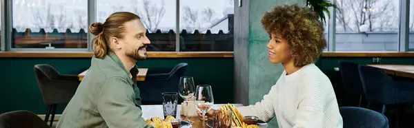 Une femme afro-américaine et un homme s'assoient gracieusement à une table dans un café moderne, engagés dans une conversation. — Photo de stock