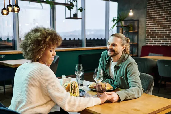 Афроамериканка и мужчина, наслаждающиеся едой в современном кафе, беседующие и смеющиеся. — стоковое фото