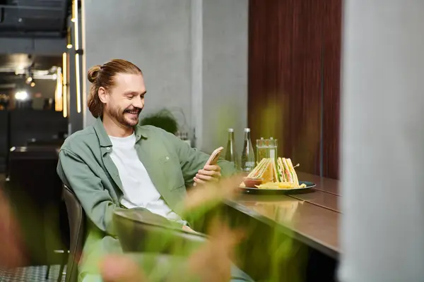 Un uomo seduto a un tavolo, che gusta un piatto di cibo in un bar moderno. — Foto stock