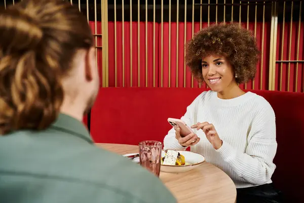 Una donna afroamericana si siede a un tavolo, gustando un piatto di cibo delizioso in un ambiente moderno caffè. — Foto stock
