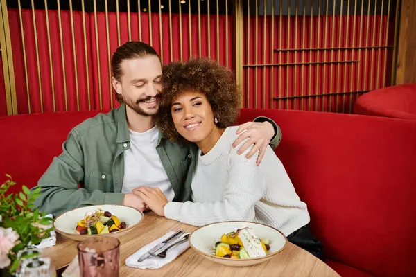 Африканська американка і чоловік сидять за столом, насолоджуючись тарілками їжі в сучасному кафе. — стокове фото
