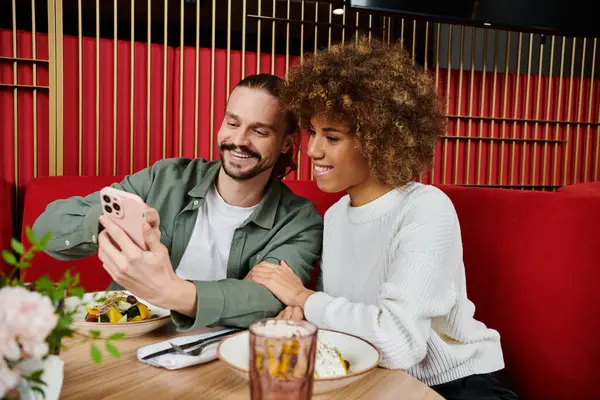 A man and African American woman sit at a table, engrossed in a cell phone. — Stock Photo