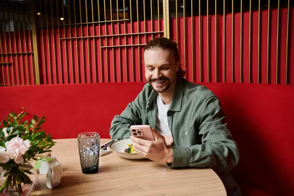 Un hombre sentado en una mesa, absorto en su celular en un café moderno. - foto de stock