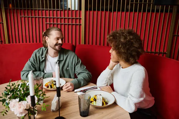 A man and an African American woman enjoy a meal together at a table in a modern cafe, with plates of delicious food in front of them. — Stock Photo