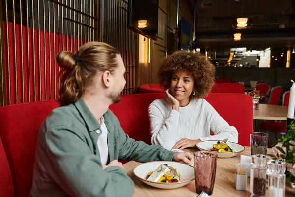 Dos mujeres elegantes disfrutan de una comida en una mesa llena de platos de deliciosa comida en un entorno de cafetería de moda. - foto de stock