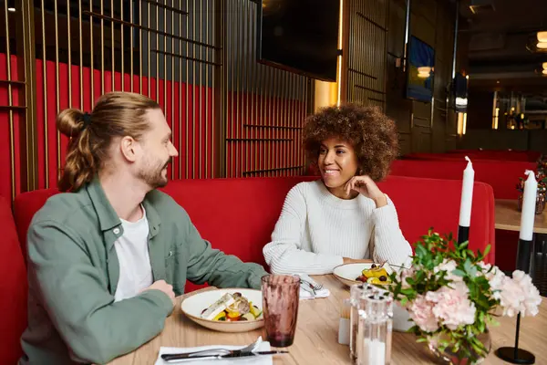 Una mujer afroamericana y un hombre disfrutan de una comida juntos en una elegante mesa de restaurante. - foto de stock
