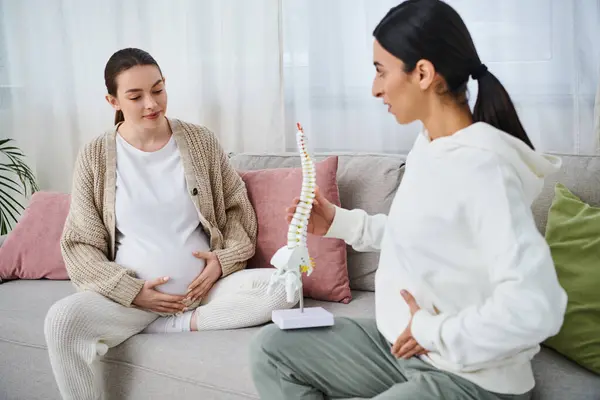 Dos mujeres, una embarazada, participan en una discusión profunda mientras están sentadas en un sofá acogedor durante un curso prenatal. - foto de stock