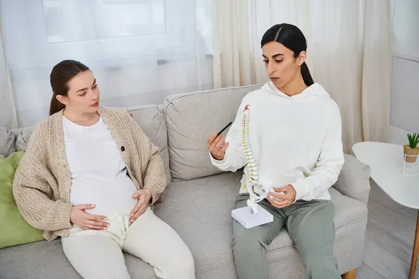Две беременные женщины ведут дружеский разговор, сидя на диване во время курса для родителей. — стоковое фото